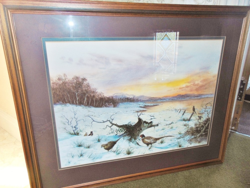 A framed winter landscape painting depicting pheasants foraging in snow beneath a sunset sky, enclosed in a dark wooden frame.