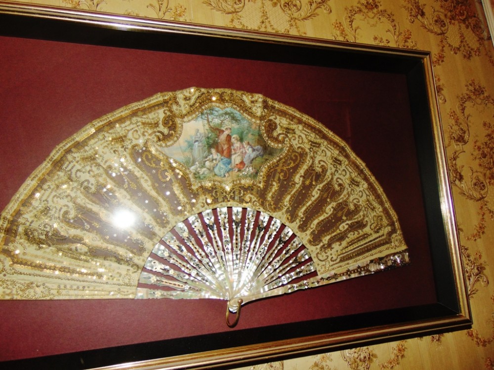 An Edwardian framed hand fan featuring iridescent mother of pearl sticks and a gold sequined lace leaf with a painted central pastoral scene.