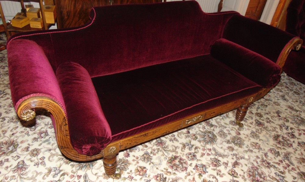 A Scottish Regency period scroll end settee upholstered in deep red velvet, featuring a carved wooden frame with turned legs and brass castors.