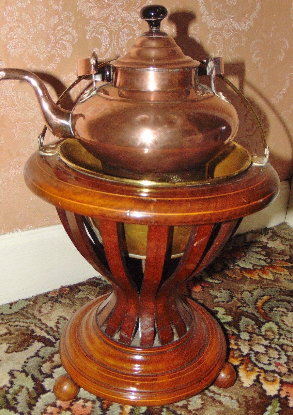 An antique mahogany tulip-shaped tea bucket featuring slatted sides, turned ball feet, a brass liner, and a fitted copper kettle.