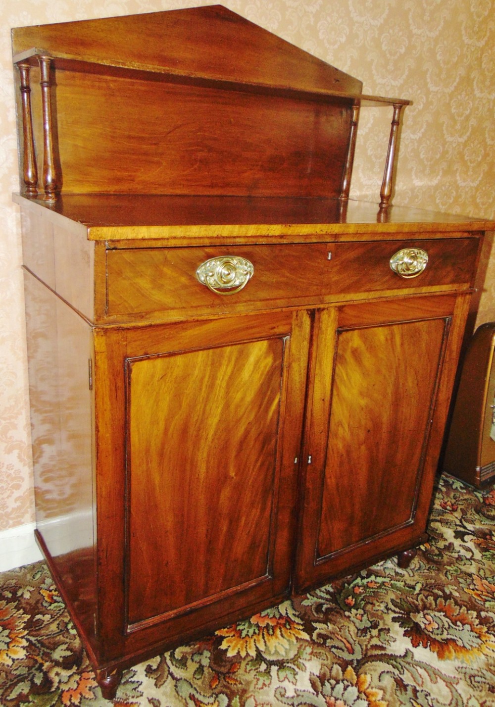 A Regency mahogany chiffonier featuring a triangular pedimented backboard with a single shelf on turned supports above a long frieze drawer and double cupboard doors.
