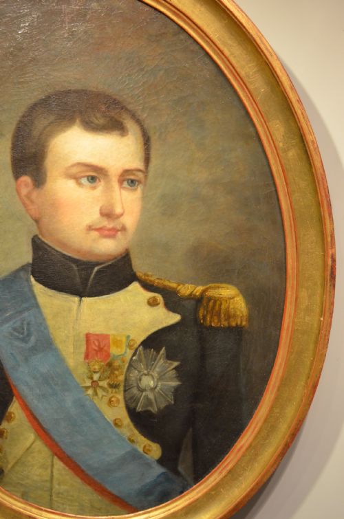fig 4. An oval oil painting depicting Napoleon Bonaparte in a dark military uniform with gold epaulettes and a light blue sash, set within a gilt wood frame.