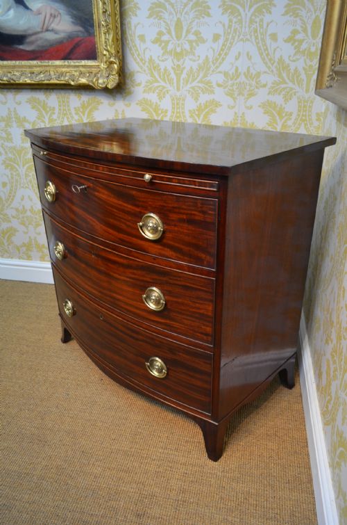 fig 1. A Regency mahogany bow-fronted chest of drawers with three graduated drawers, brass lion-head ring handles, line inlay, and splayed bracket feet.