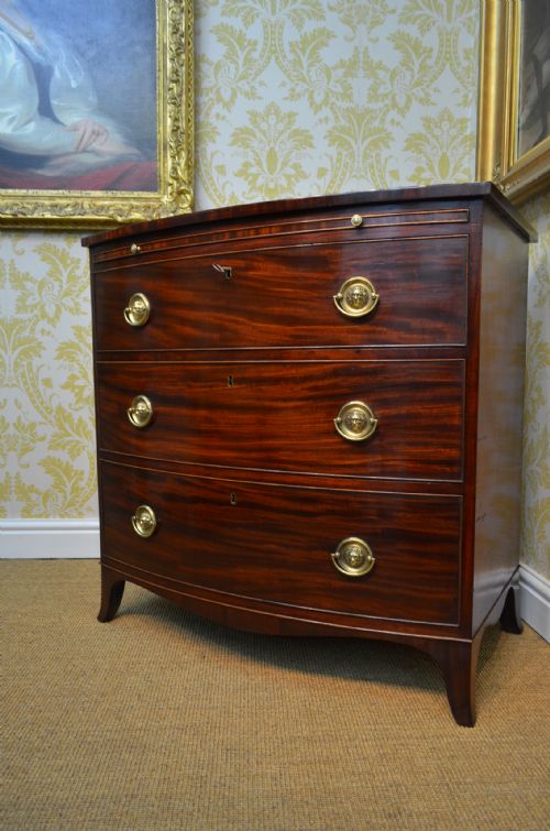 fig 2. A Regency mahogany bow-fronted chest of drawers with three graduated drawers, brass lion-head ring handles, line inlay, and splayed bracket feet.