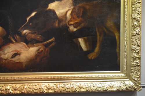 fig 4. An oil painting depicting two dogs reaching into a woven basket containing meat and fruit, encased in an ornate gilded frame.