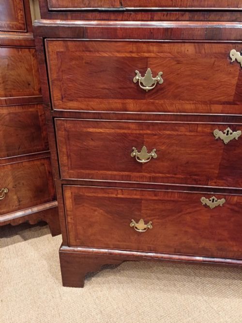 fig 1. An early eighteenth-century walnut chest on chest featuring crossbanded drawers, brass handles, and bracket feet.