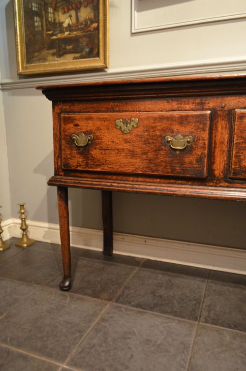 fig 1. An 18th-century George III oak dresser base featuring three drawers with decorative brass handles and supported on slender legs with pad feet.
