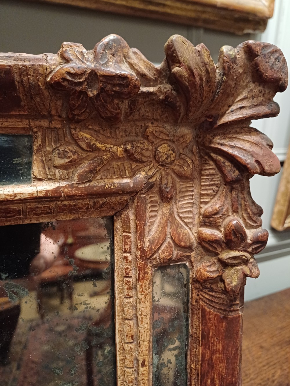 A small rectangular French Regence carved wooden mirror featuring floral motifs and inset glass slips surrounding an aged central mirror plate. View VI
