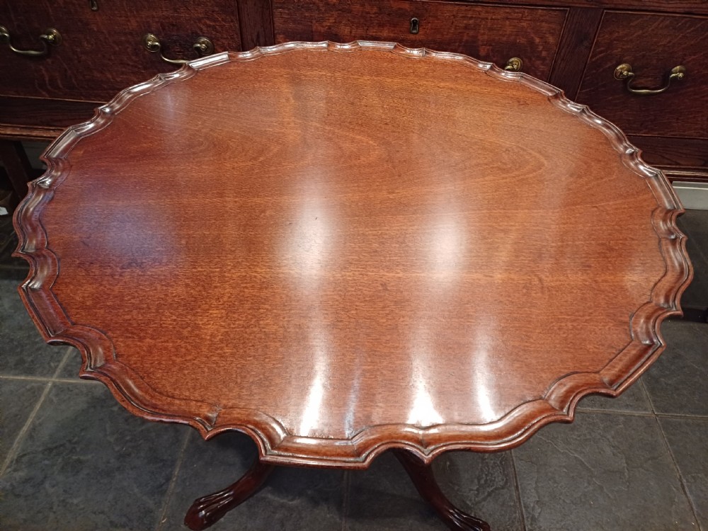 An 18th-century mahogany tilt-top table positioned vertically to display a carved piecrust border, turned pillar, and tripod cabriole legs. View II