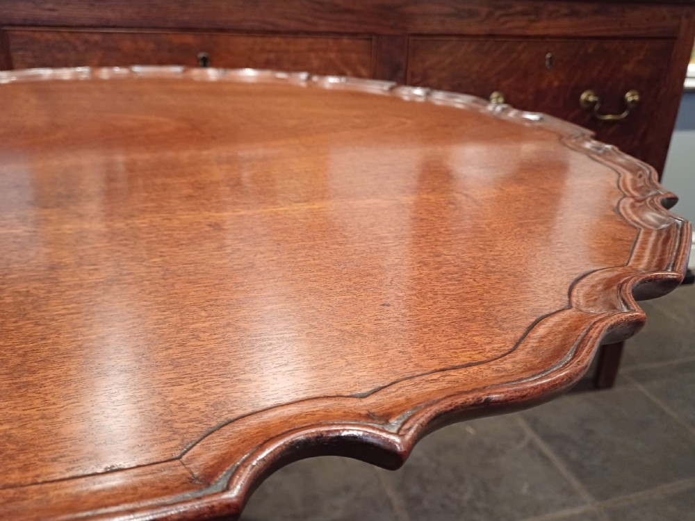 An 18th-century mahogany tilt-top table positioned vertically to display a carved piecrust border, turned pillar, and tripod cabriole legs. View VI