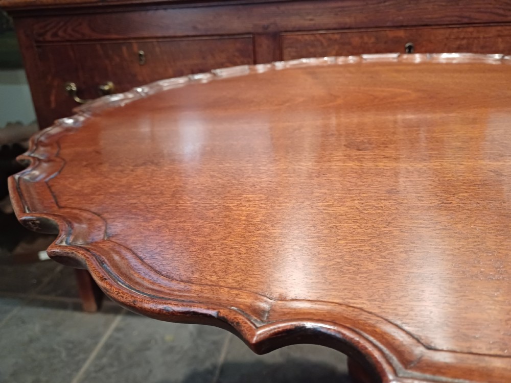 An 18th-century mahogany tilt-top table positioned vertically to display a carved piecrust border, turned pillar, and tripod cabriole legs. View VII