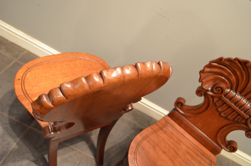 A pair of early 19th-century Regency mahogany hall chairs featuring shell-carved cresting, solid seats, and turned front legs. View XI