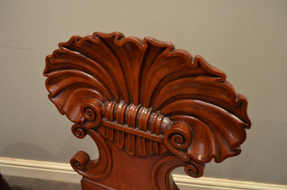 A pair of early 19th-century Regency mahogany hall chairs featuring shell-carved cresting, solid seats, and turned front legs. View XIII