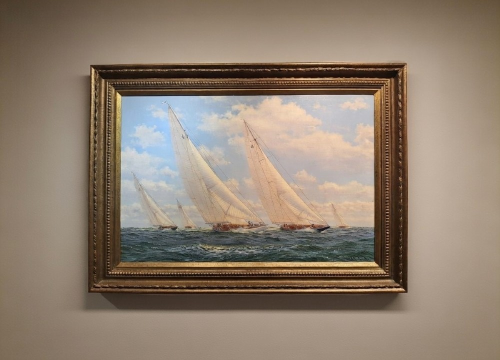 A gilt-framed oil painting depicting classic racing yachts sailing through choppy blue seas under a cloudy sky.