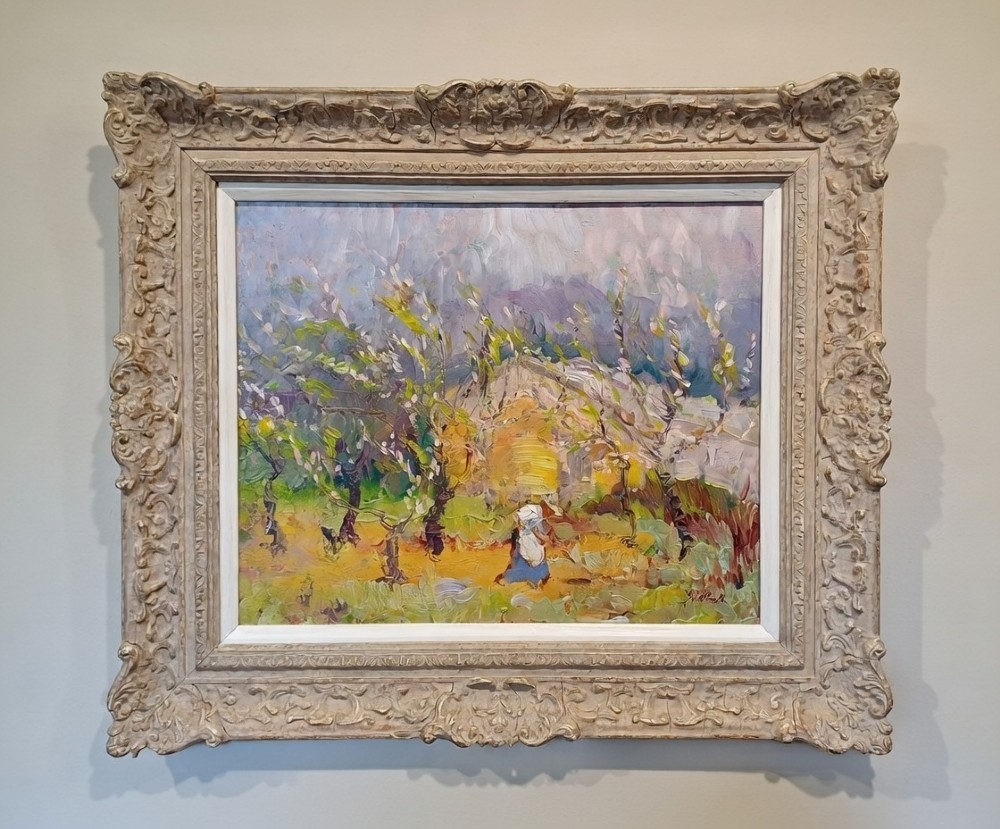 An impressionist oil painting on panel depicting figures amidst blossoming trees set inside an ornate carved swept frame.