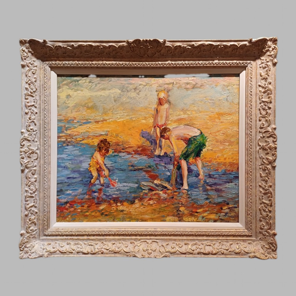 An impressionist oil painting depicting three children playing in shallow water on a sunny beach, enclosed in an ornate swept frame.