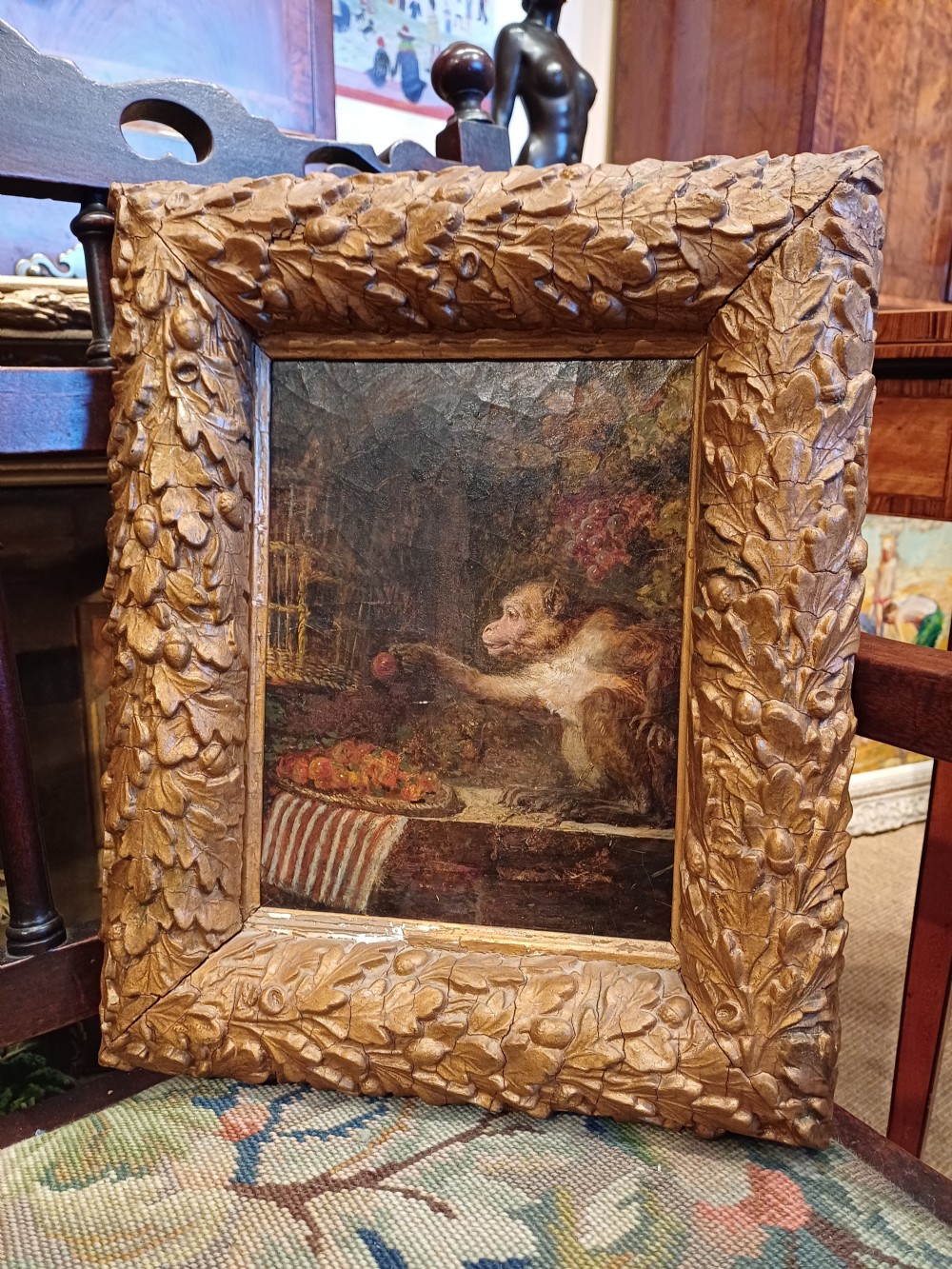 A 19th-century oil painting depicting a monkey beside fruit, enclosed within an ornate, hand-carved giltwood frame featuring oak leaf and acorn motifs. View IX