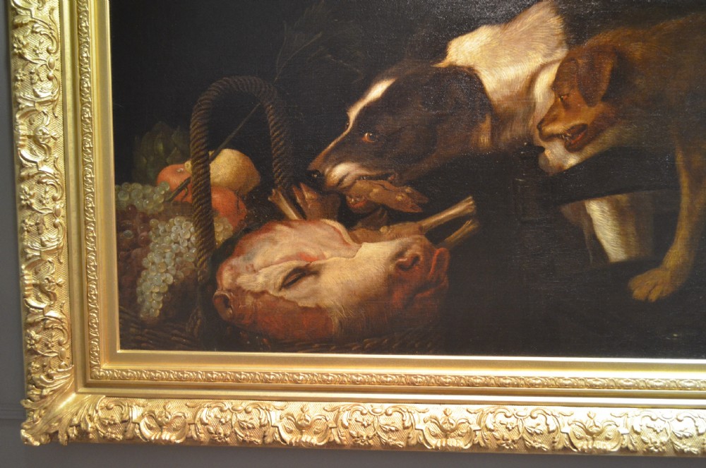 An oil painting depicting two dogs reaching into a woven basket containing meat and fruit, encased in an ornate gilded frame. View IV