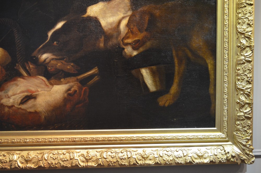 An oil painting depicting two dogs reaching into a woven basket containing meat and fruit, encased in an ornate gilded frame. View V