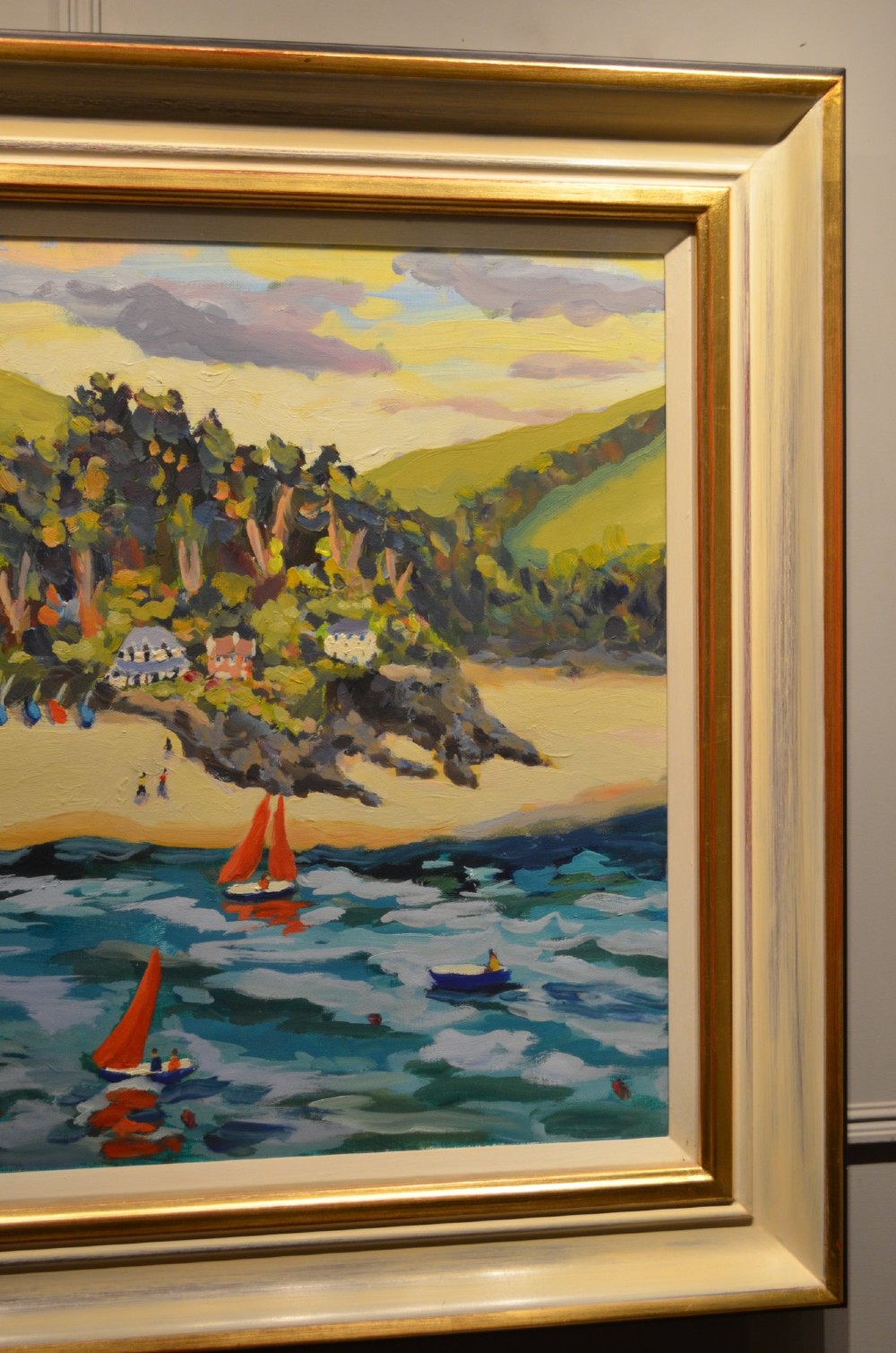 A framed oil painting on canvas depicting boats with red sails on blue water before a sandy shore and green hills. View III