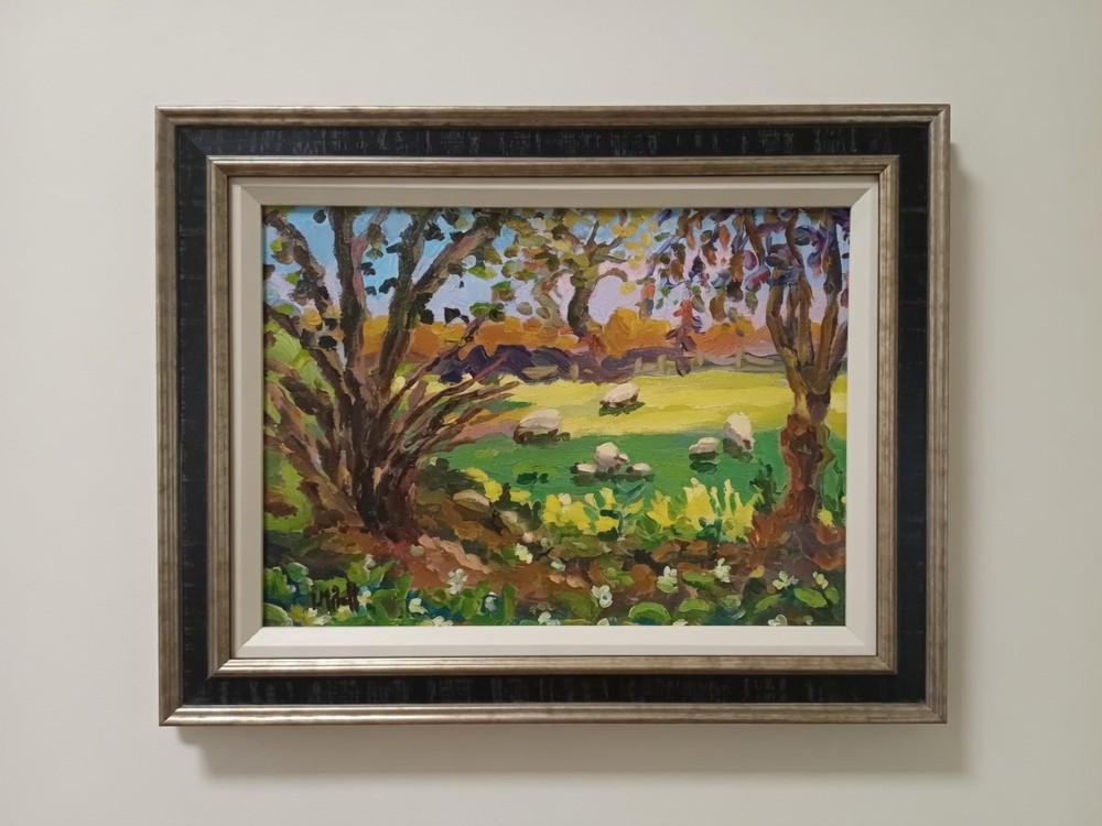 A framed impressionist oil painting on canvas depicting sheep grazing in a field of wild garlic under trees.