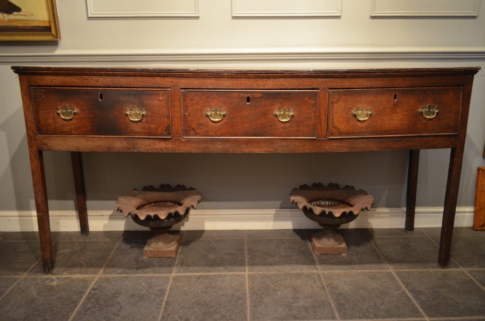 A Georgian solid oak dresser base featuring three drawers with brass swan-neck handles, supported by four straight square legs. View VIII