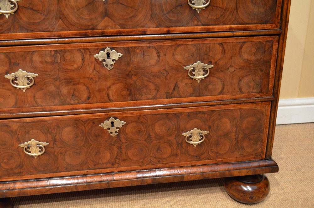 An antique William and Mary period walnut chest of drawers featuring geometric oyster veneer patterns, brass teardrop handles, keyhole escutcheons, and turned bun feet. View V