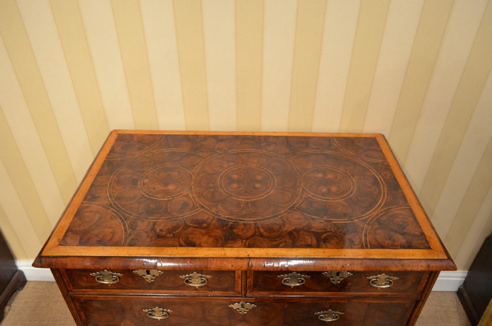 An antique William and Mary period walnut chest of drawers featuring geometric oyster veneer patterns, brass teardrop handles, keyhole escutcheons, and turned bun feet. View VII