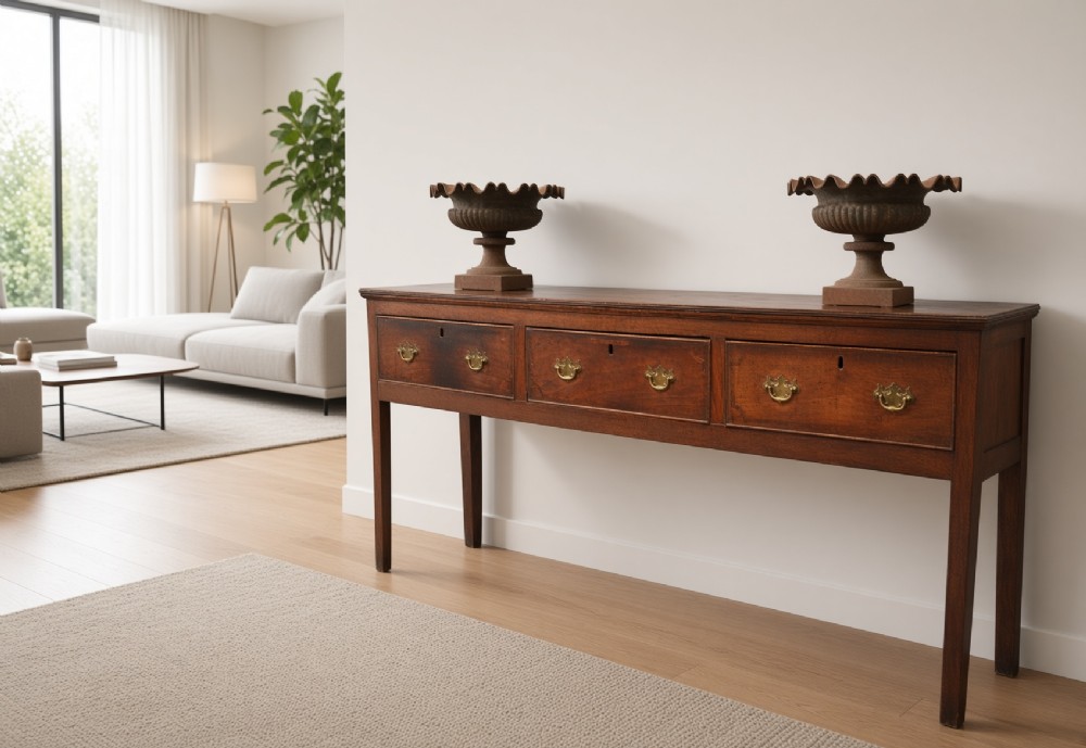A Georgian solid oak dresser base featuring three drawers with brass swan-neck handles, supported by four straight square legs. View XI