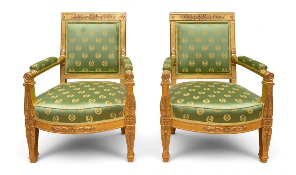 A pair of 19th-century French giltwood armchairs featuring carved classical motifs and green silk upholstery patterned with gold laurel wreaths.