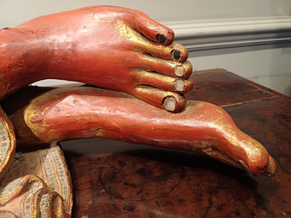 A 19th-century Burmese carved wooden sculpture of a reclining Buddha featuring red lacquered finish and detailed gilded robes. View V