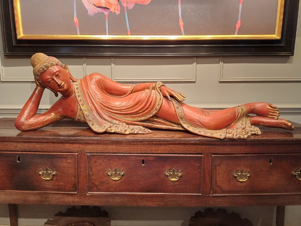 A 19th-century Burmese carved wooden sculpture of a reclining Buddha featuring red lacquered finish and detailed gilded robes. View IX