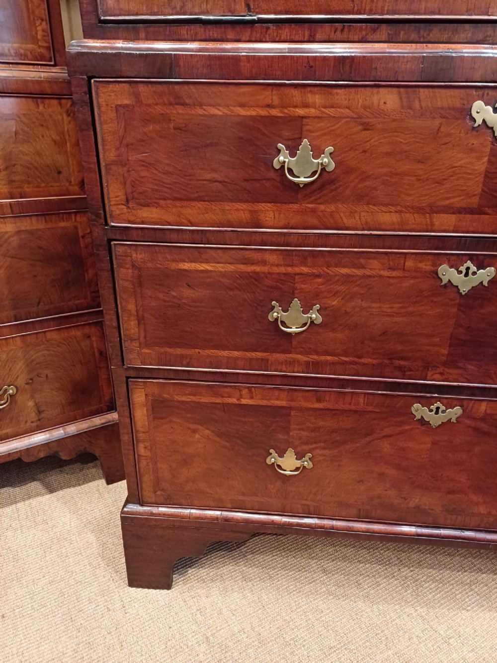 An early eighteenth-century walnut chest on chest featuring crossbanded drawers, brass handles, and bracket feet. View II