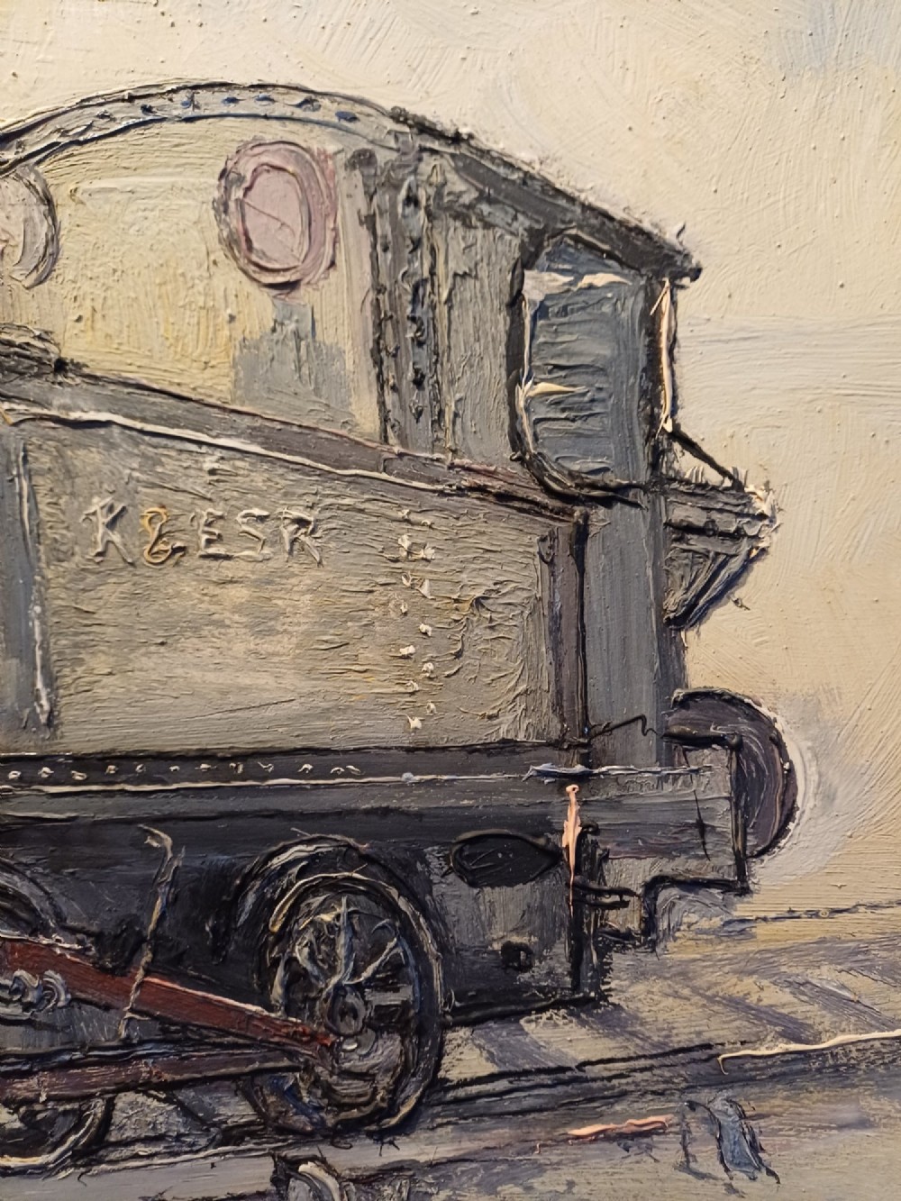 An original oil painting on board depicting a dark grey and red side tank steam locomotive sitting on railway tracks, presented in a light wooden frame with a wide mount. View XI