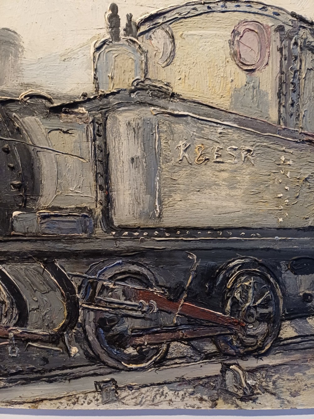 An original oil painting on board depicting a dark grey and red side tank steam locomotive sitting on railway tracks, presented in a light wooden frame with a wide mount. View XII