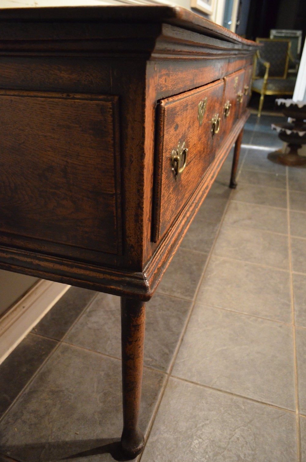 An 18th-century George III oak dresser base featuring three drawers with decorative brass handles and supported on slender legs with pad feet. View XII
