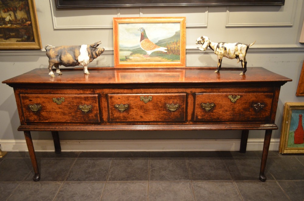 An 18th-century George III oak dresser base featuring three drawers with decorative brass handles and supported on slender legs with pad feet. View XIII