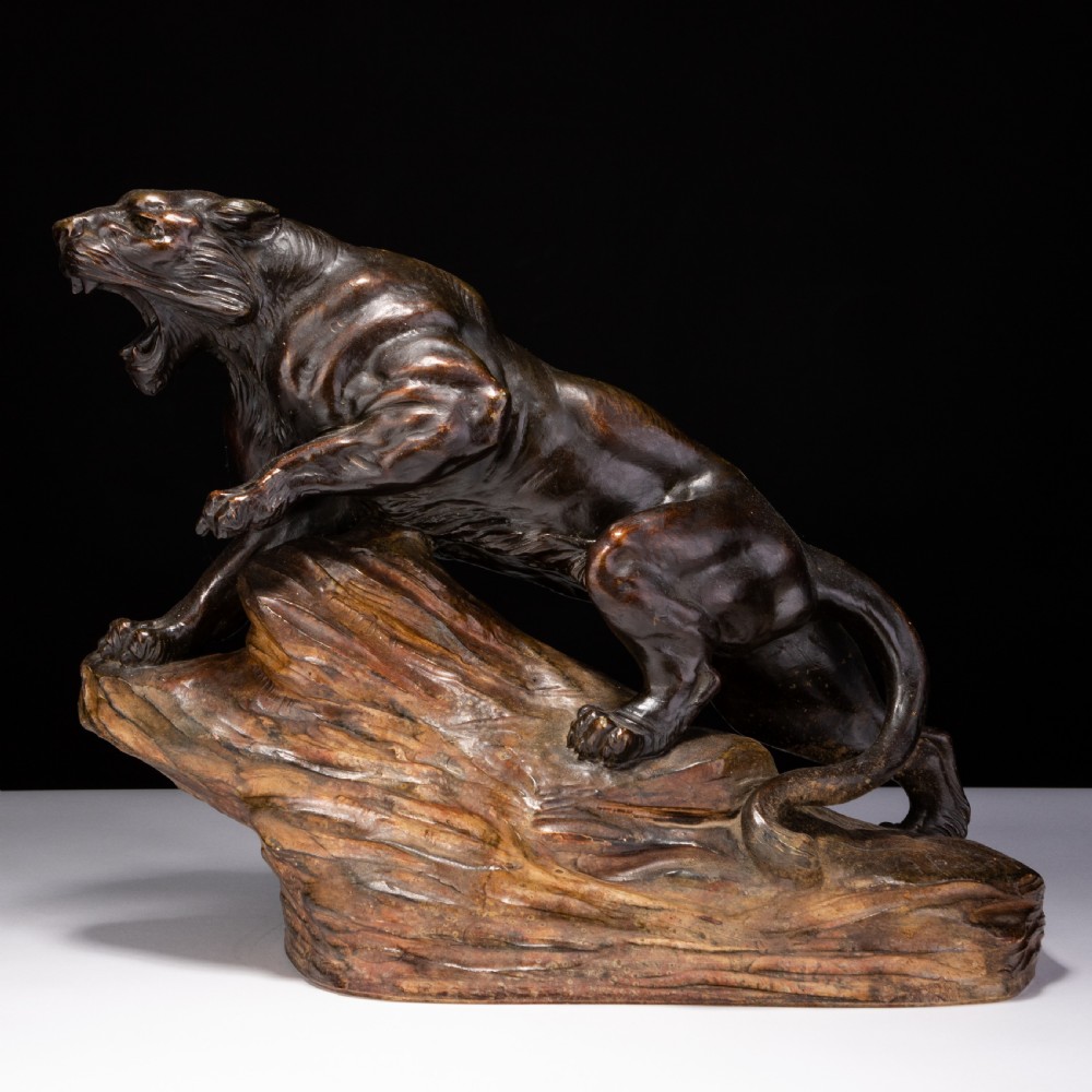 A dark brown patinated ceramic sculpture depicting a roaring tiger poised on a rocky base in the Art Deco style.
