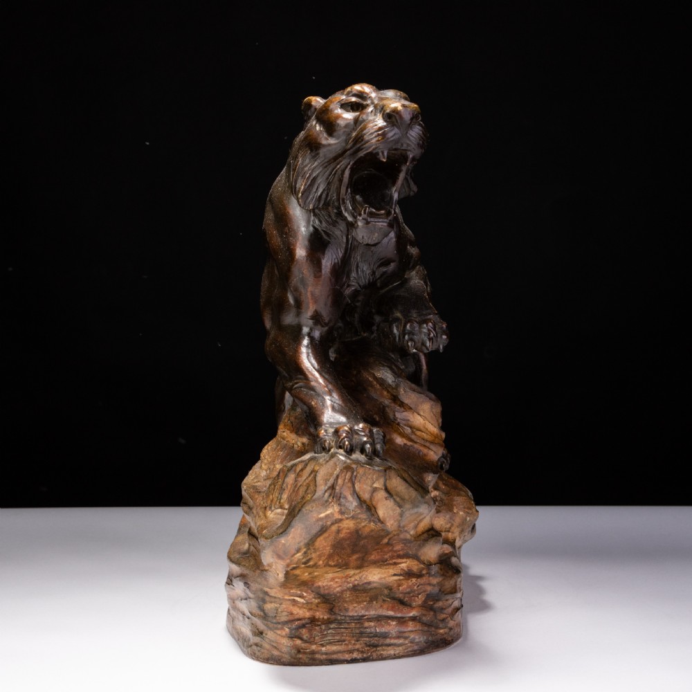 A dark brown patinated ceramic sculpture depicting a roaring tiger poised on a rocky base in the Art Deco style. View II