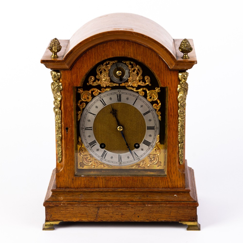 An antique dome-top oak mantel clock featuring gilded bronze corner accents, pinecone finials, and a brass dial with a silvered chapter ring.