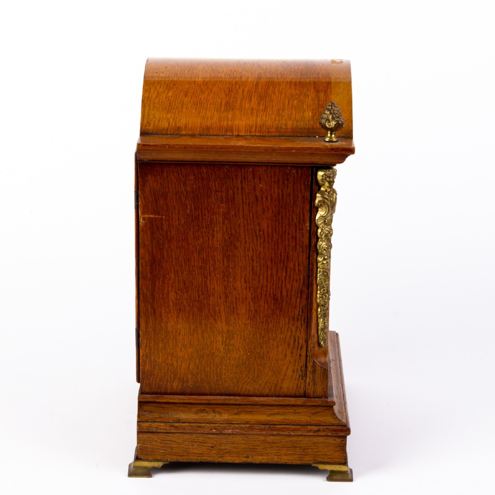 An antique dome-top oak mantel clock featuring gilded bronze corner accents, pinecone finials, and a brass dial with a silvered chapter ring. View II