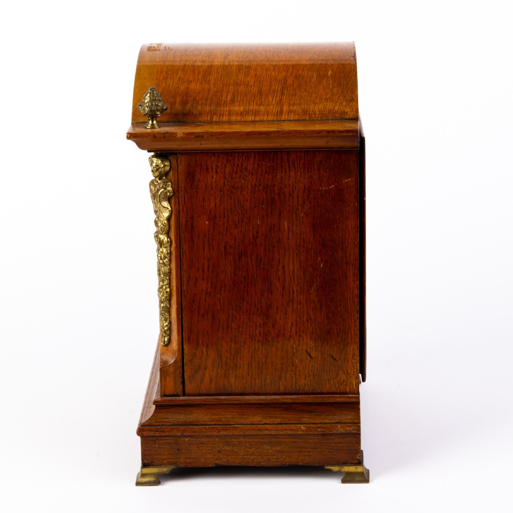 An antique dome-top oak mantel clock featuring gilded bronze corner accents, pinecone finials, and a brass dial with a silvered chapter ring. View III