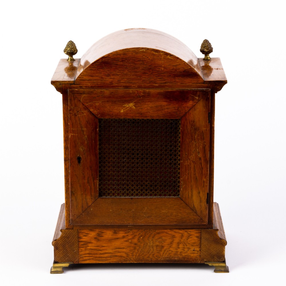 An antique dome-top oak mantel clock featuring gilded bronze corner accents, pinecone finials, and a brass dial with a silvered chapter ring. View IV