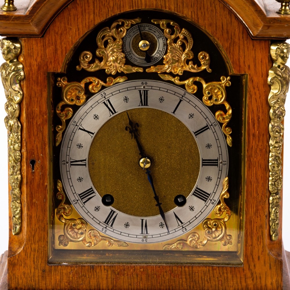 An antique dome-top oak mantel clock featuring gilded bronze corner accents, pinecone finials, and a brass dial with a silvered chapter ring. View VI