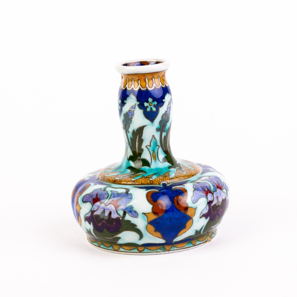 A squat, bulbous ceramic vase featuring an elongated neck, painted with polychrome Art Nouveau floral patterns in shades of blue, turquoise, orange, and purple against a white glaze.