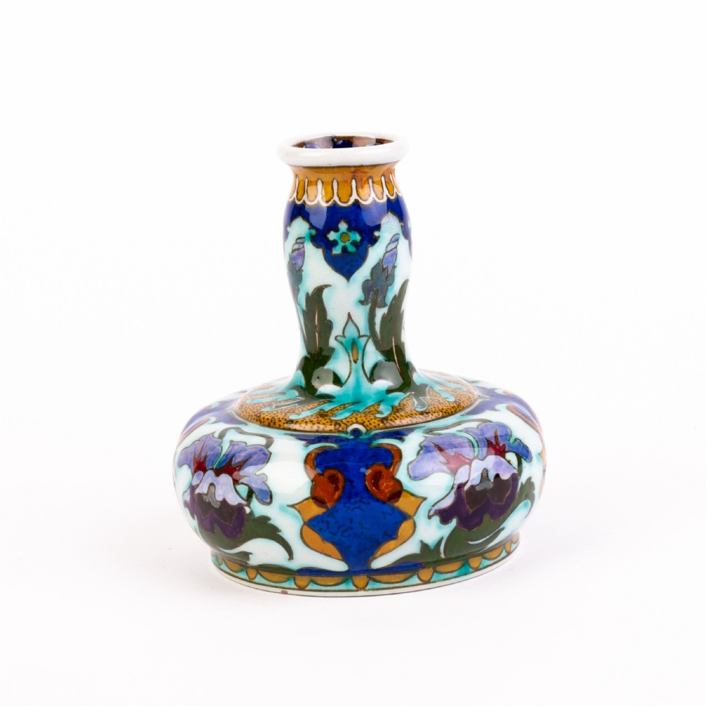 A squat, bulbous ceramic vase featuring an elongated neck, painted with polychrome Art Nouveau floral patterns in shades of blue, turquoise, orange, and purple against a white glaze. View V