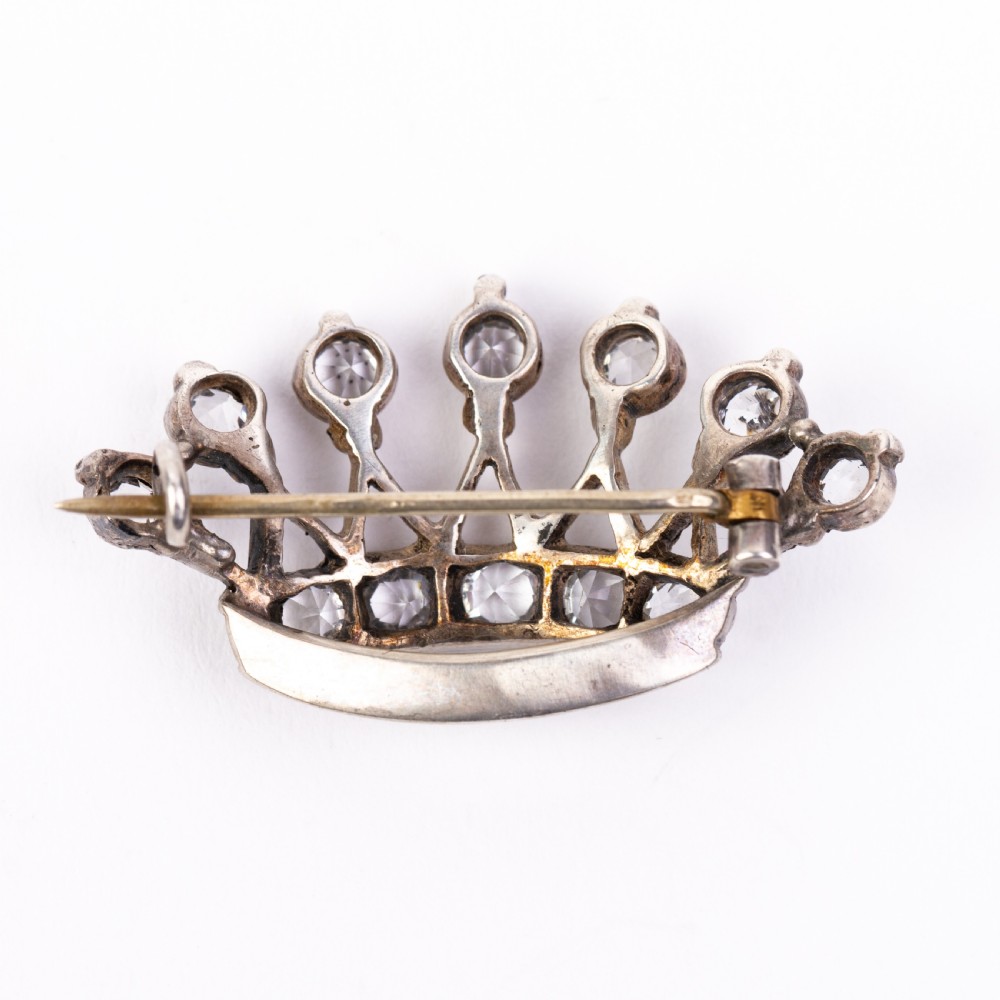 A Victorian silver brooch designed in the shape of a crown and set with round clear paste stones along the band and points. View V