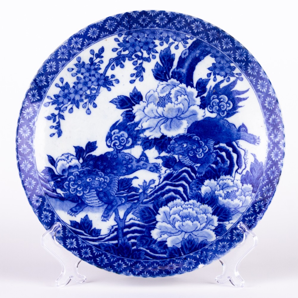 A circular blue and white Chinese porcelain display plate painted with Foo dogs and peony flowers encircled by a decorative patterned border.
