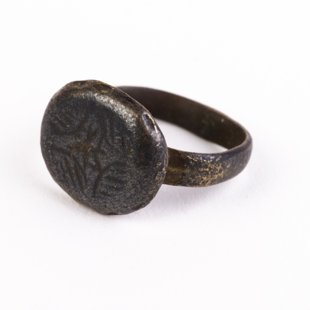 A dark patinated bronze signet ring featuring a rounded bezel hand-engraved with an eight-pointed star motif on a narrow metal band.