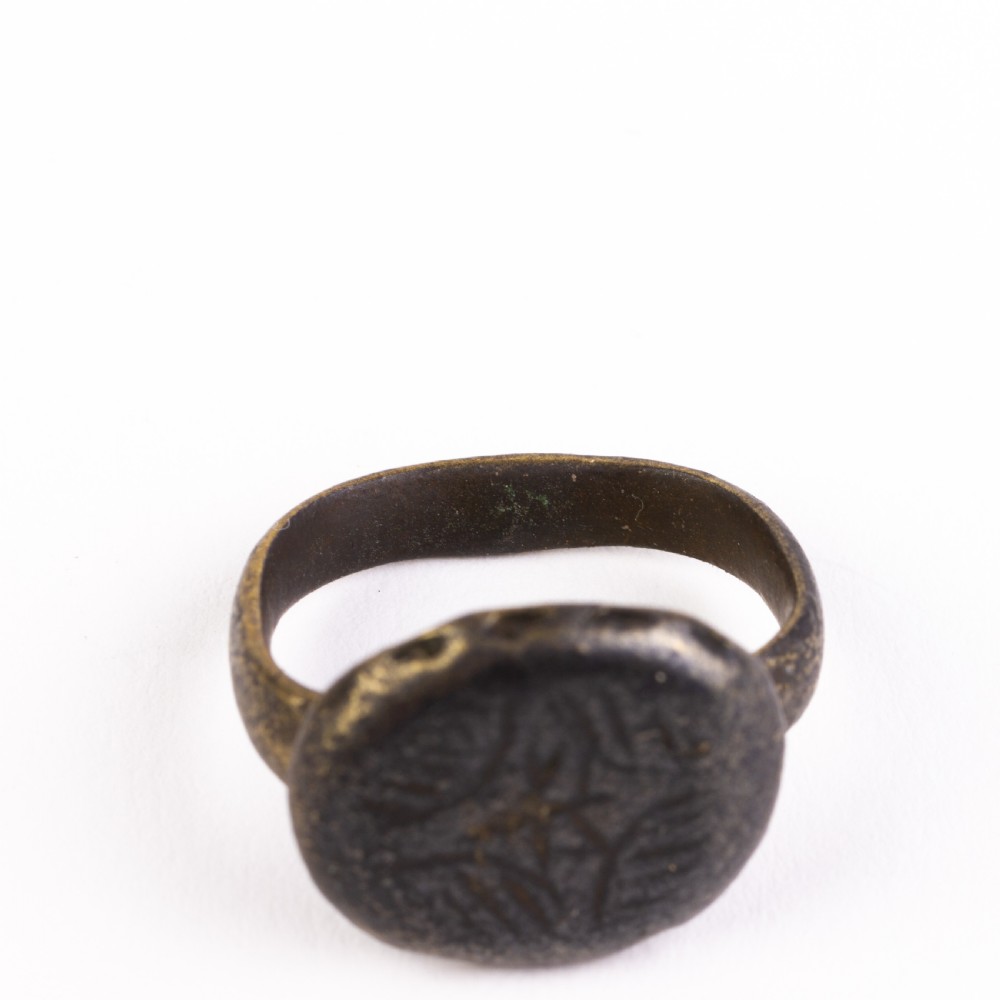 A dark patinated bronze signet ring featuring a rounded bezel hand-engraved with an eight-pointed star motif on a narrow metal band. View V